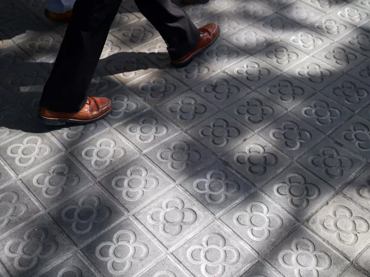 Pies caminando por una acera con baldosas características de Barcelona